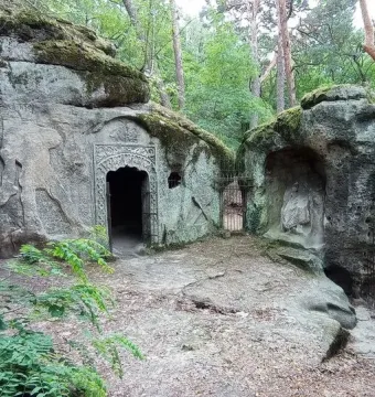 Klácelka rock cave with a dark arched entrance and a gated stone alcove in the forest.