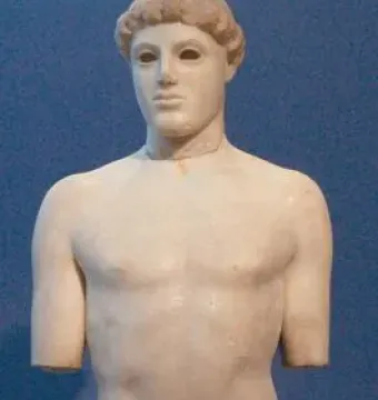 Kritios Boy, a nude marble statue with short curly hair and damaged arms against a blue background.