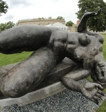 La Rivière by Aristide Maillol, a dark reclining female sculpture on a stone base in a garden setting.