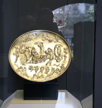The Parabiago Plate displayed upright in a museum case, showing a detailed high-relief mythological scene on a circular metal dish.