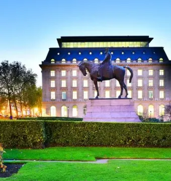 Leopold II equestrian statue on a stone pedestal in front of a neoclassical building at dusk.