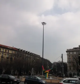 Needle, Thread and Knot sculpture rising from a Milan roundabout, with colorful ribbons wrapped around its base.