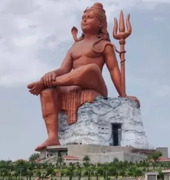 The Statue of Belief, a massive seated Shiva statue with a cobra and trident on a large base under a cloudy sky.