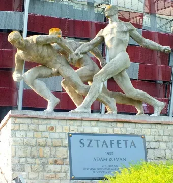 Sztafeta sculpture showing three nude male figures passing a baton on a stone base.
