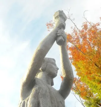 Victims of Communism Memorial statue viewed from below, with the female figure raising an object overhead against a bright sky and autumn leaves.
