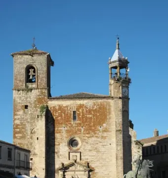 Francisco Pizarro equestrian statue partly visible behind palm fronds, with a stone church in the background.