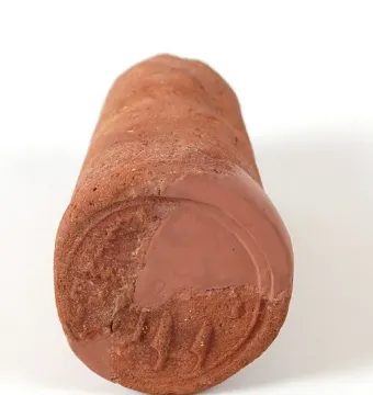 Reddish-brown funerary cone with a partially preserved circular impression and relief carvings on one flattened end.