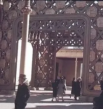 Ornate architectural tower interior with decorative latticework and panels, with people walking below.