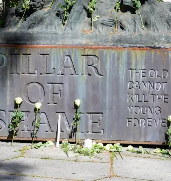 The Pillar of Shame base with white roses and candles arranged around the memorial inscription.