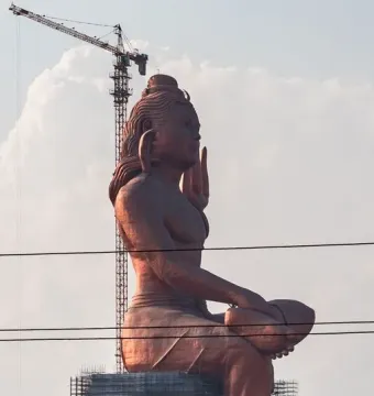 The Statue of Belief rises above scaffolding, with a crane behind it and power lines in the foreground.