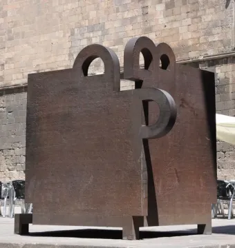 Topos V by Eduardo Chillida in front of a stone building with a pointed arch window and café tables nearby.