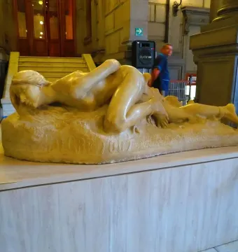 Malgré Tout, a reclining unclothed female sculpture with bound ankles on a textured base.