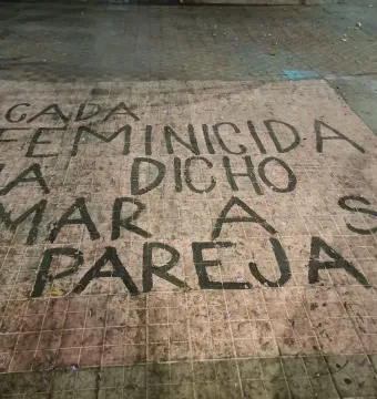 Painted Spanish text on a tiled surface at The Roundabout of the Disappeared reads “Cada feminicida ha dicho amar a su pareja.”