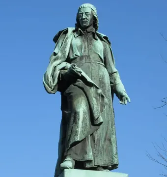 The Vodnik Monument shows a weathered green statue of a man in a long robe holding a rolled document on a stone pedestal.