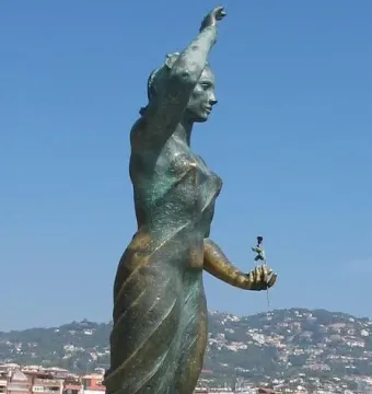Dona Marinera bronze sculpture of a woman standing on a rock with one arm raised and a flower in her other hand.
