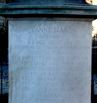 Close-up of the Joan of Arc statue pedestal with a French engraved inscription in capital letters.