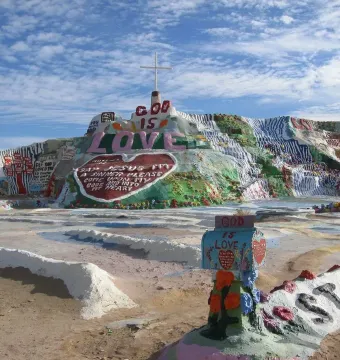 Salvation Mountain with colorful painted stripes, large hearts, religious messages, and a white cross on top.