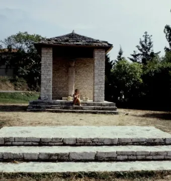 U Nativu stone monument under an open-air pavilion with a seated person at its base