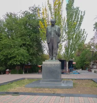 Monument to Avetik Isahakyan in a tree-lined public square with benches and small kiosks nearby