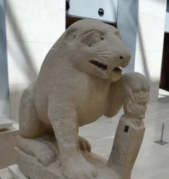 Bear of Porcuna stone sculpture with one paw resting on a herma topped by a carved head.