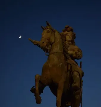 The Equestrian Statue of Louis XIV silhouetted against a deep blue evening sky with a crescent moon above.
