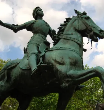 Joan of Arc bronze equestrian statue with a raised sword against a cloudy sky.