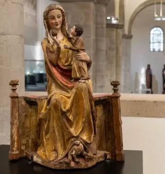 Virgin on a Wide Throne, a painted wooden sculpture of a seated woman holding a child and raising a round fruit.