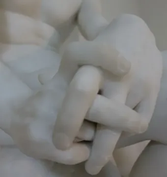 Clasped marble hands from The Exiled, with part of the figure’s arms and torso visible.