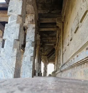 A long stone corridor with massive carved pillars and bright light at the far end.