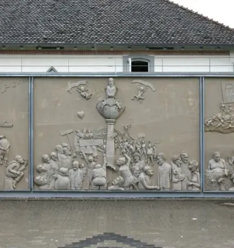 Ludwigs Erbe stone relief with three panels showing a crowded central monument scene and smaller figures on either side.