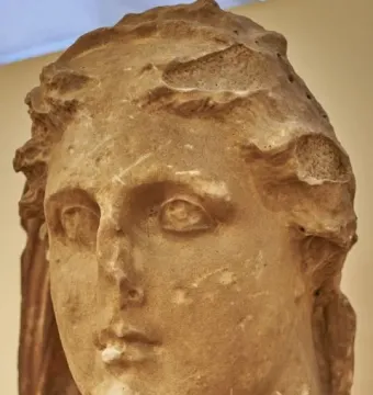 Colossal head of Demeter with wavy hair and worn stone surface on a pedestal.