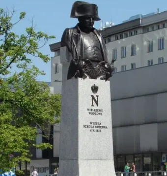 Bronze bust of Napoleon I on a tall stone plinth with engraved symbols and wreaths at the base.