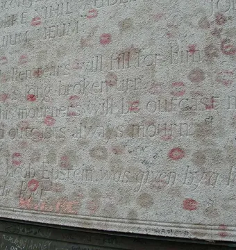 Inscribed stone section of Oscar Wilde\'s tomb covered with lipstick kiss marks and graffiti.