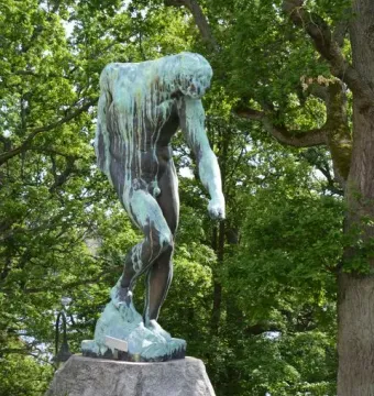 The Shade bronze sculpture of a nude male figure leaning forward on a rock in a garden setting.