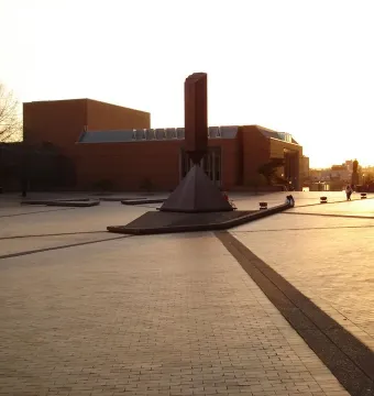 Broken Obelisk sculpture in a paved plaza with brick buildings in the background.