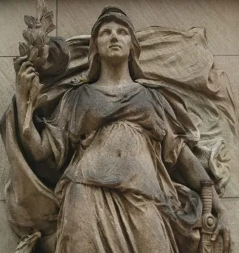 Weathered stone relief on the Commodore John Barry Statue showing a draped female figure with a head covering, holding a leafy branch and resting a hand on a sword hilt.
