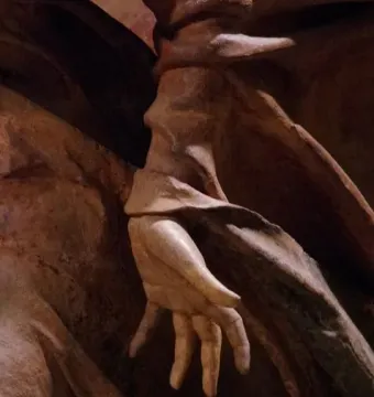Close-up of a sculpted hand from Compianto sul Cristo morto, surrounded by dark draped folds.