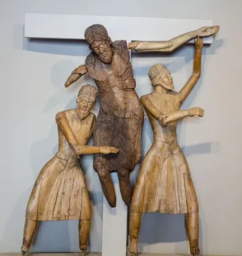 Descent from the Cross wooden sculpture showing three figures before a white cross as two bearded men in pleated robes support the central body.