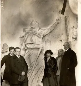 A group of five people stands around a large sculpture of Mickiewicz in a workshop, with other busts and reliefs on the walls.