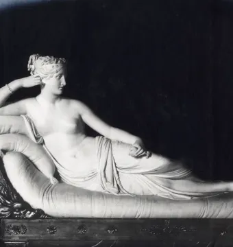 Venus Victrix, a white marble sculpture of a reclining female figure on an ornate chaise lounge, holding an object in one hand.