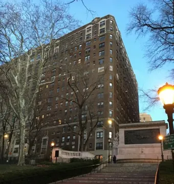Firemen\'s Memorial beside a wide brick stairway, with lampposts, bare trees, and a tall brick apartment building in the background.