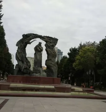 Huseyn Javid Monument with a central robed figure holding a staff, set on a stone base in a park.