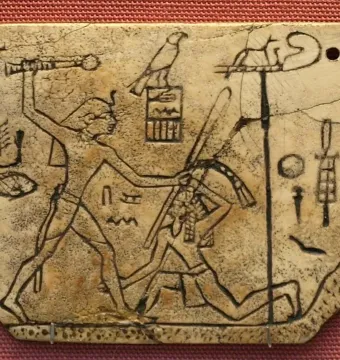MacGregor plaque showing a cracked ivory carving of a standing figure raising a mace over a kneeling figure, with hieroglyphs and a standard.