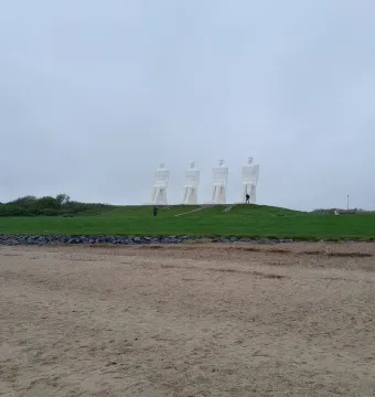 The Man by the Sea sculpture with four large white seated figures on a grassy mound above a sandy beach.