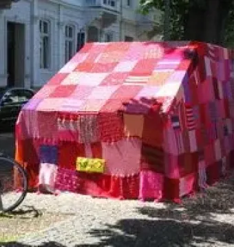Ruhender Verkehr, a vehicle covered in a colorful knitted textile blanket on a city street.