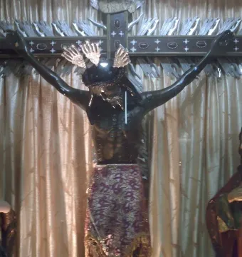 San Juan Patrón crucifix with a dark-skinned Christ statue, flanked by a veiled woman and a bearded man.