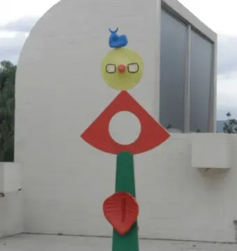 The Caress of a Bird sculpture with stacked colorful abstract shapes on a green pillar.