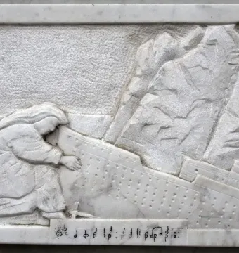 Detail of the Titanic Musicians\' Memorial showing a white marble relief of a kneeling figure reaching toward a listing ship, with musical notation below.