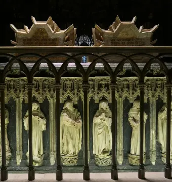 Tomb of Charles III and Eleanor with carved robed figures in niches and an ornate upper section, partly obscured by a metal railing.