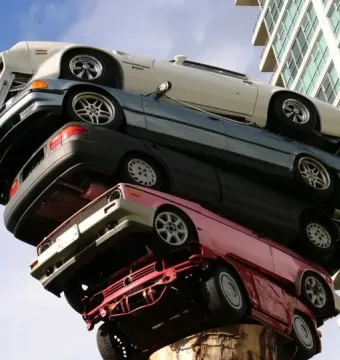 Trans Am Rapture sculpture with cars stacked vertically against a blue sky and a high-rise building.